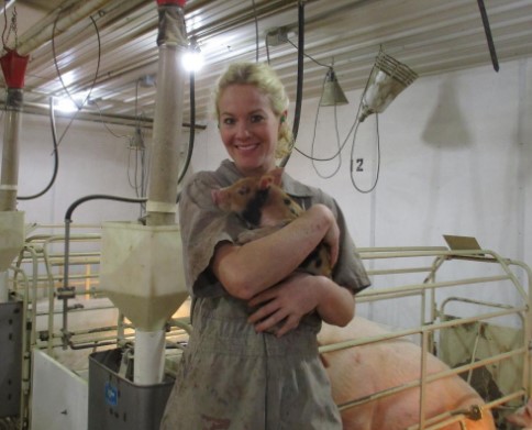 A woman standing inside a pig barn and holding a piglet 