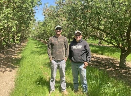 Rob Schuh and son-in-law Andrew Carroll standing in their almond orchard