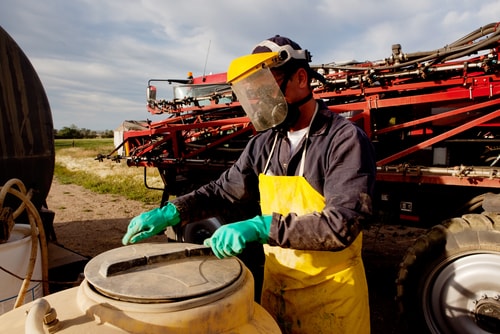 A farmer wears protective equipment while working on machinery